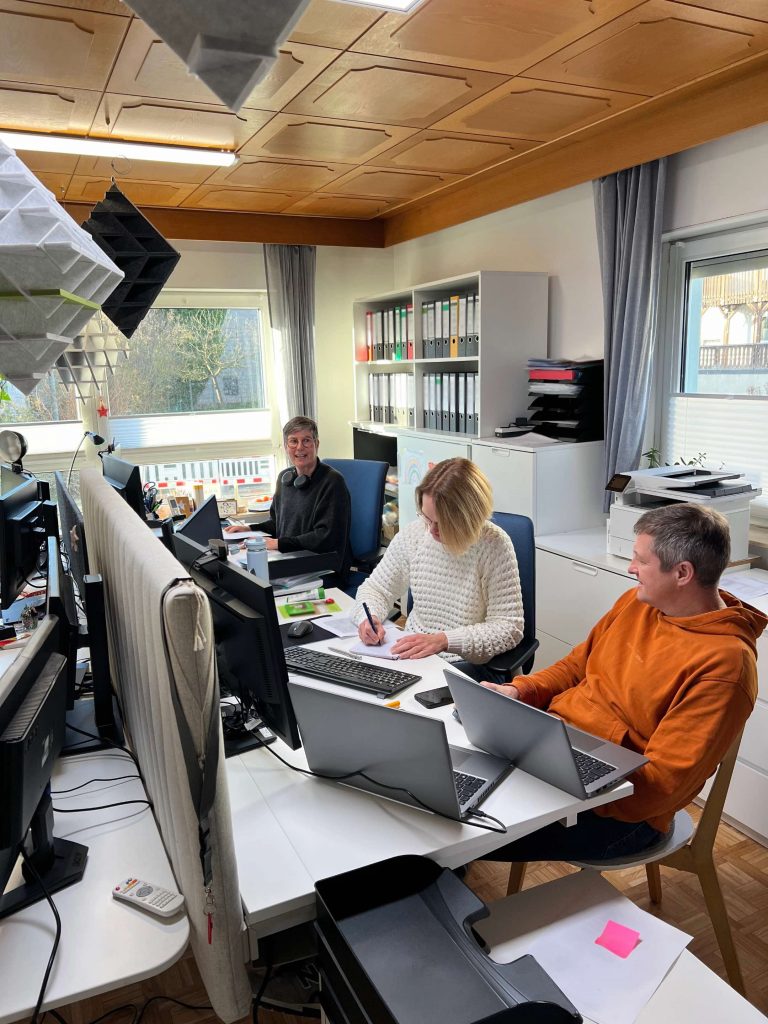 Drei Personen arbeiten im Büro und unterhalten sich währendessen.