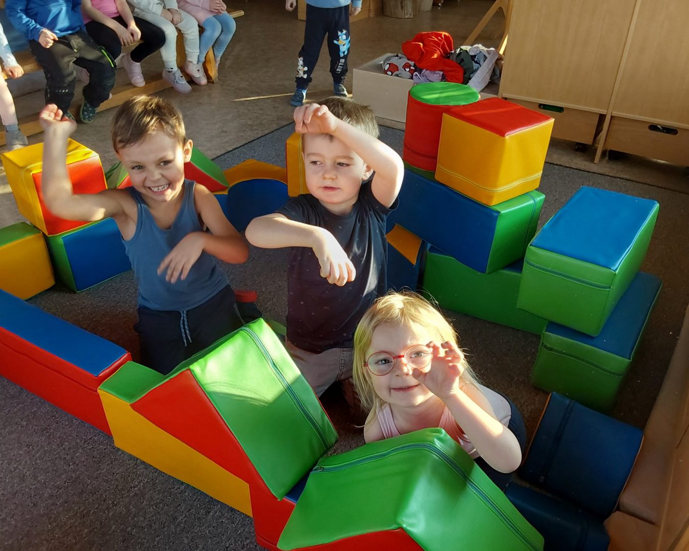 Kinder sitzen in einer selbstgebauten Burg aus großen Stoff-Bauklötzen und machen Grimassen.
