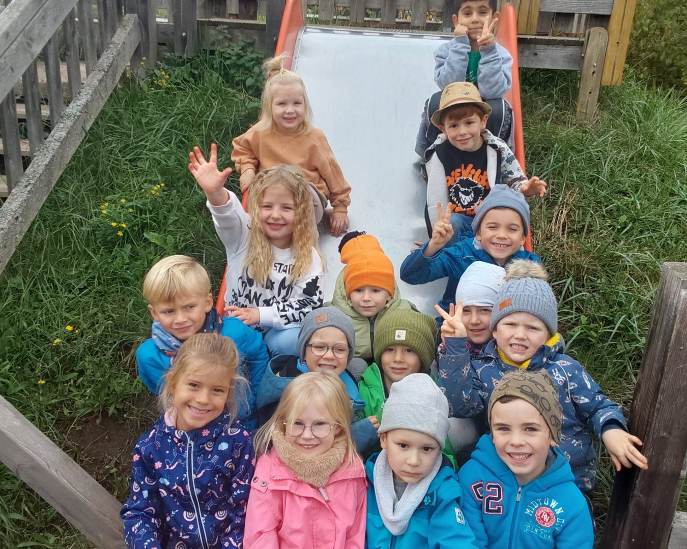 Kindergartenkinder sitzen draußen auf einer Rutsche und schauen lächelnd in die Kamera