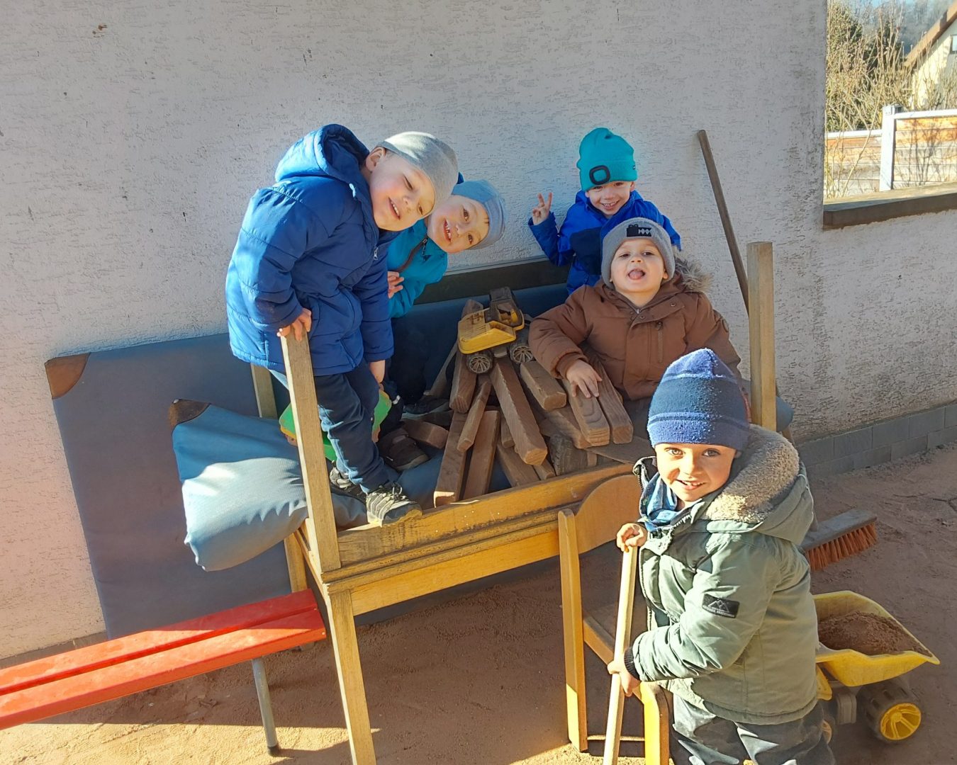 Kinder spielen im Sand mit Baufahrzeugen und lächeln in die Kamera.