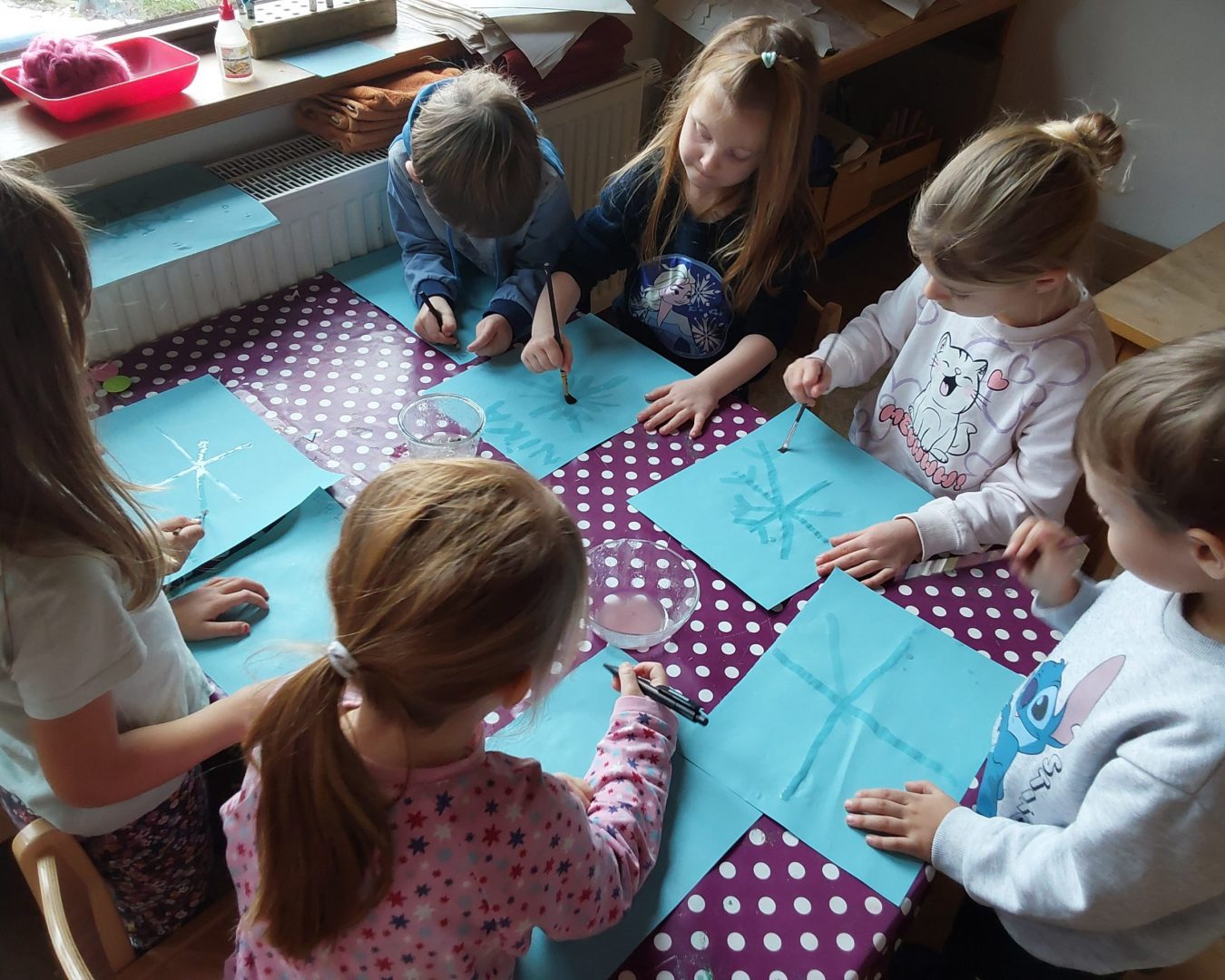 Kinder Malen Schneeflocken mit Wasser auf blauem Papier.