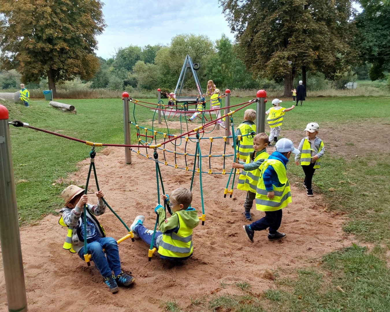 Kinder spielen auf einem Spielplatz und tragen eine Warnweste.